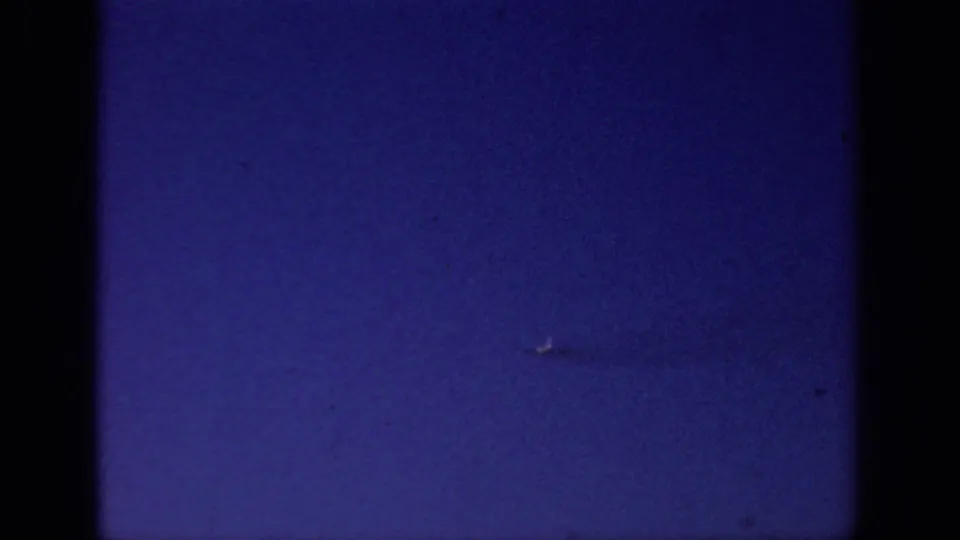 Grainy 8mm frame from Sacramento metadata showing a small pale object against blue sky and pronounced film-edge vignetting.