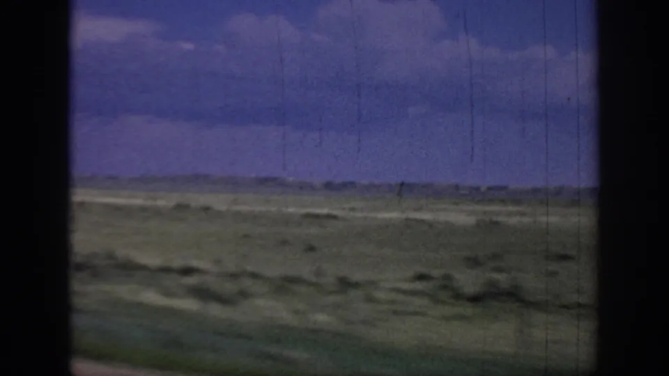 1967 Oklahoma 8mm road footage showing flat green-brown prairie from inside a moving vehicle, with a low horizon, clouded blue-purple sky, and dark window edges.
