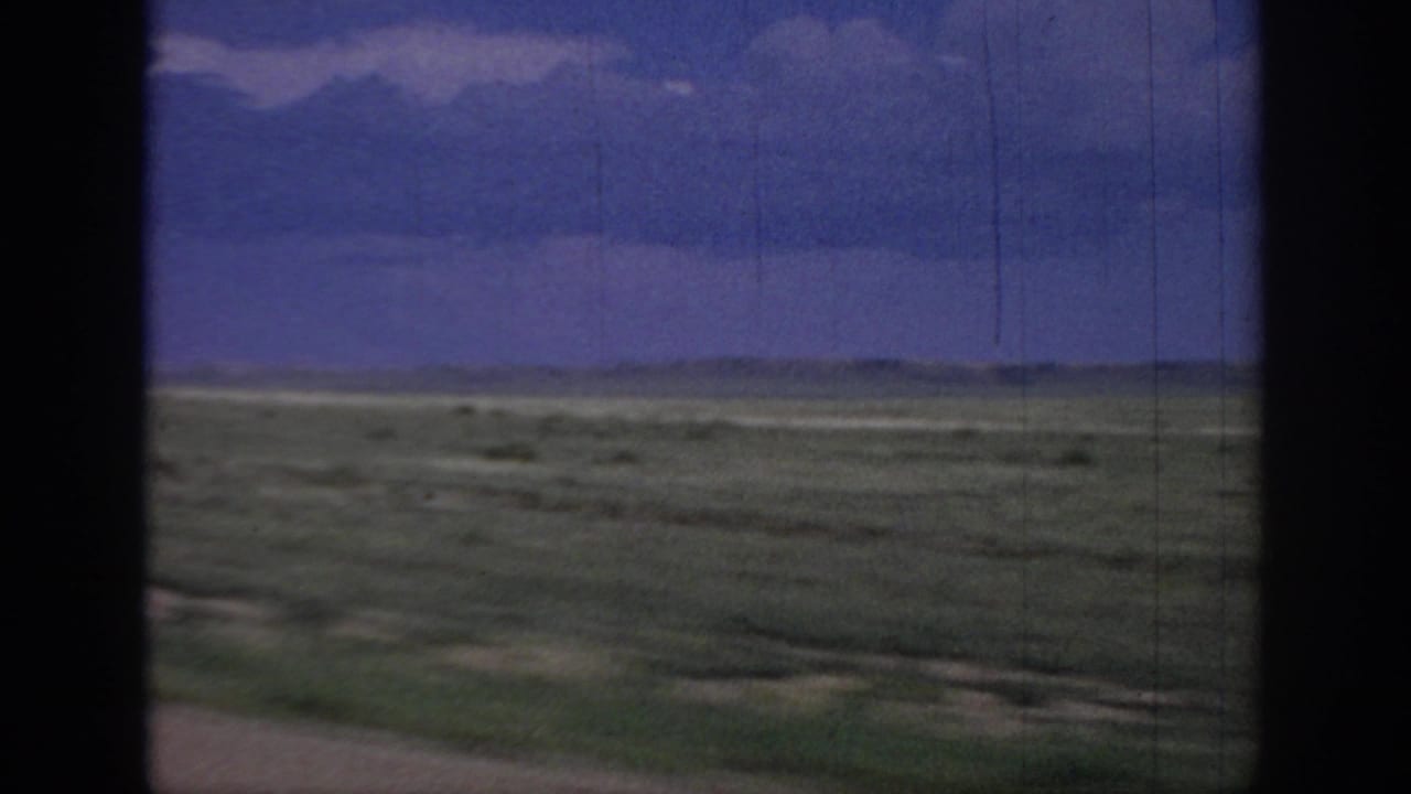 Open grassland and distant horizon viewed from a moving vehicle.