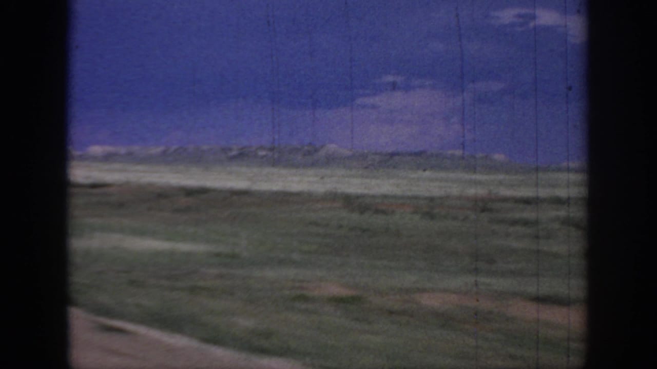 1967 Oklahoma road-trip view of open plains, low horizon, blue sky, and dark window framing from a moving vehicle.