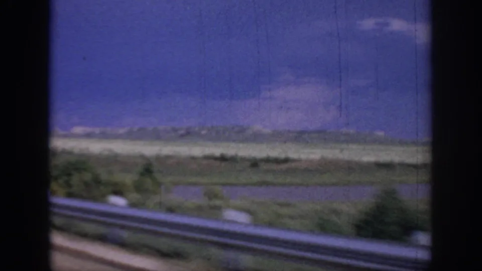 1967 Oklahoma travel frame showing roadside guardrail, flat fields, blue sky, and dark car-window borders.