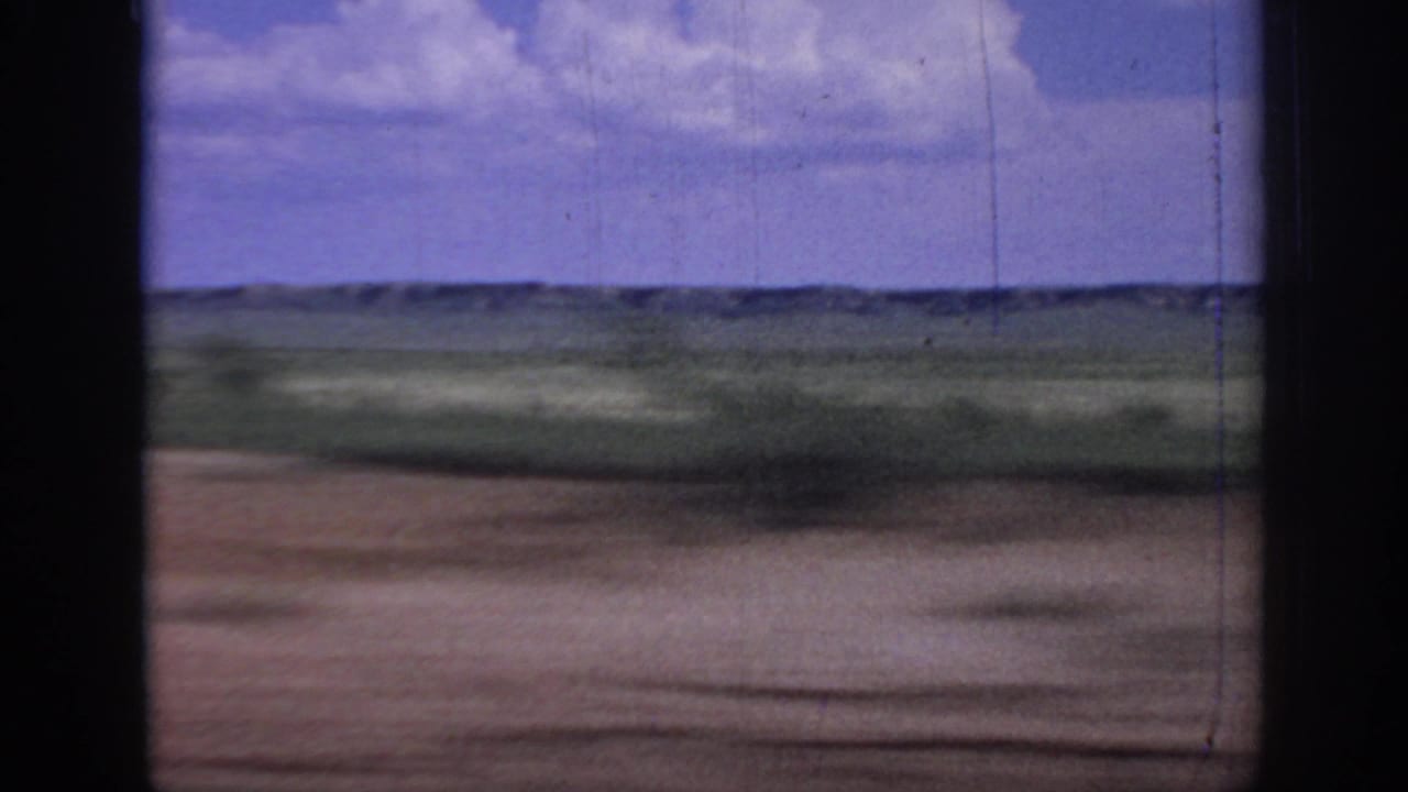 1967 Oklahoma road-view footage shows flat fields and a distant horizon through a dark vehicle window frame.