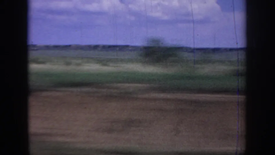 Moving 8mm view across Oklahoma fields, with window borders framing a low horizon and clouded sky.