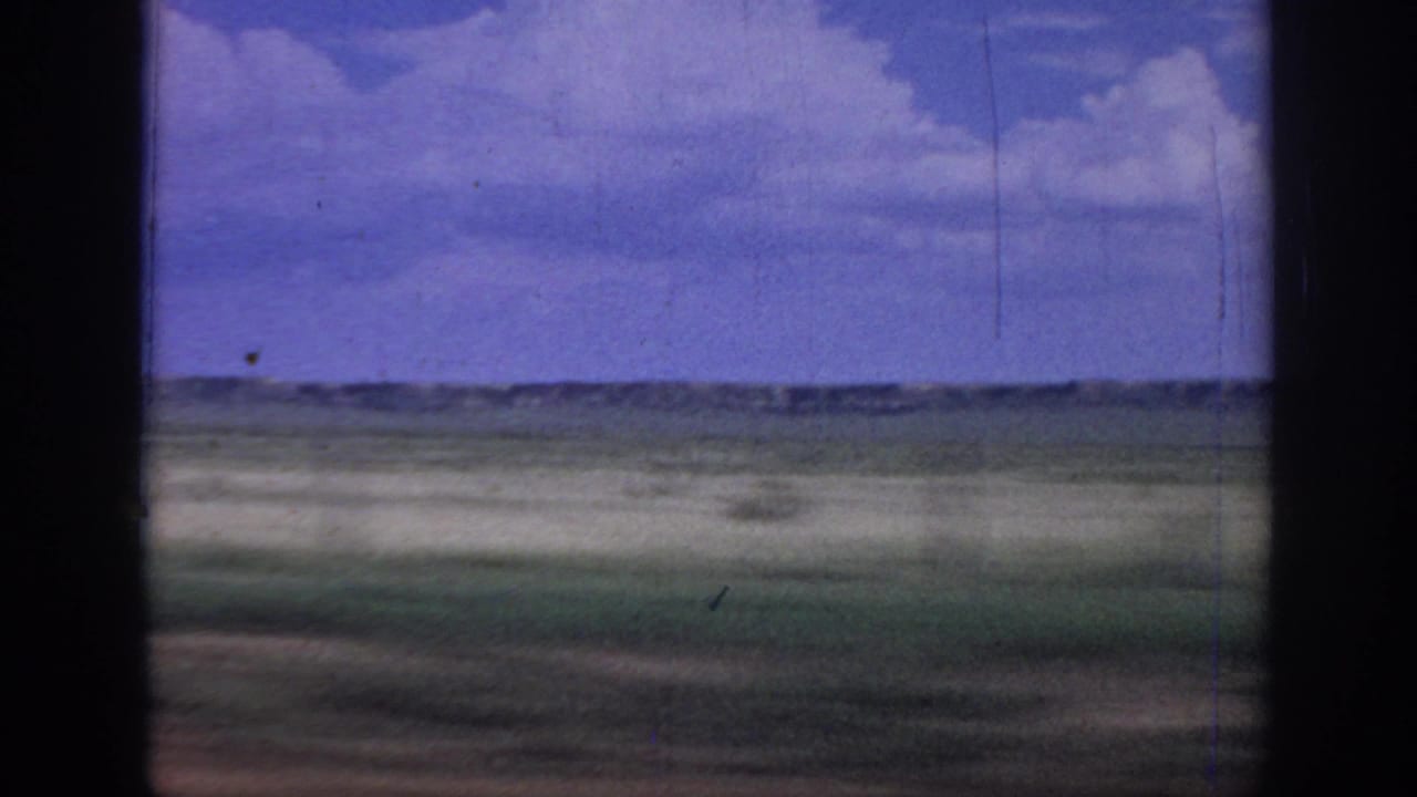 Rural Oklahoma landscape from a moving car window, with flat fields, sky, and visible 8mm wear.
