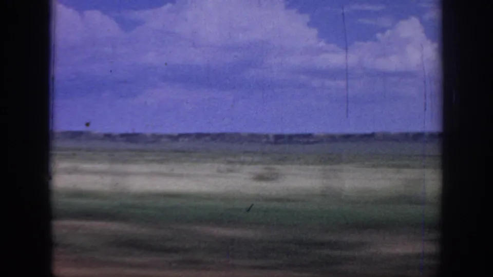 Rural Oklahoma landscape from a moving car window, with flat fields, sky, and visible 8mm wear.