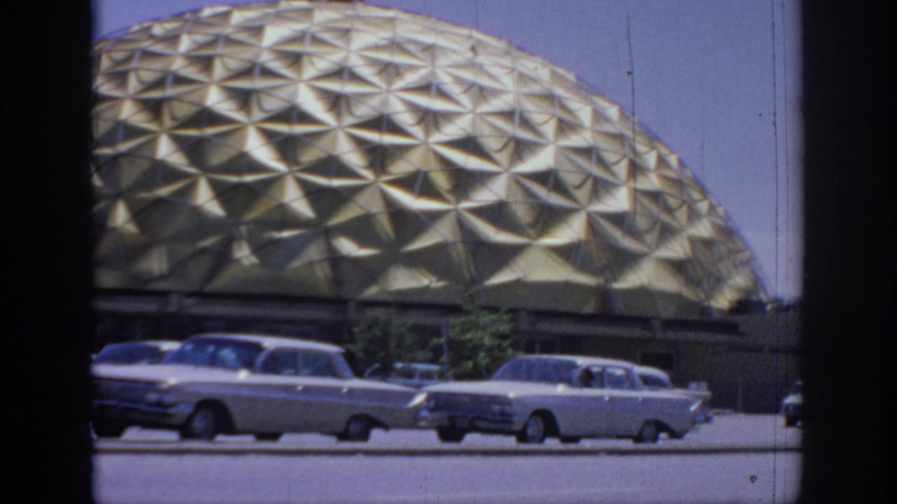 A fixed 8mm view of the gold dome in Oklahoma, with late-1960s sedans moving along the foreground street.