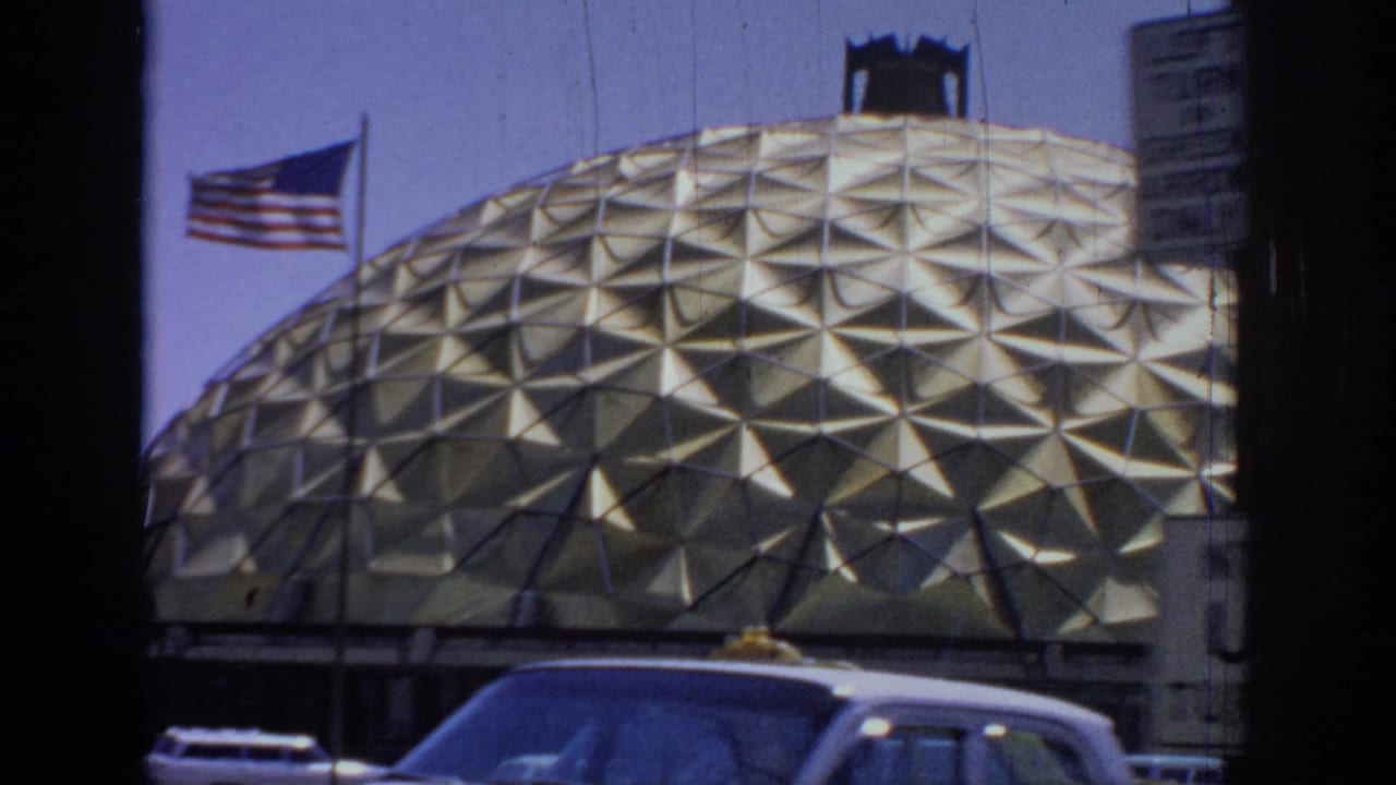 1967 Oklahoma frame with an American flag beside the gold dome, street traffic below, and a partial sign at the right edge.