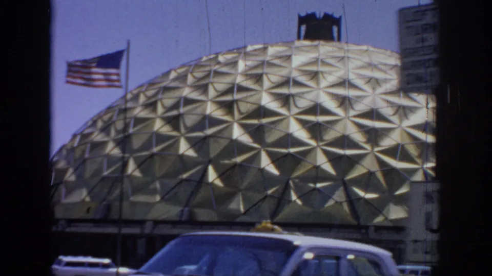 1967 Oklahoma frame with an American flag beside the gold dome, street traffic below, and a partial sign at the right edge.