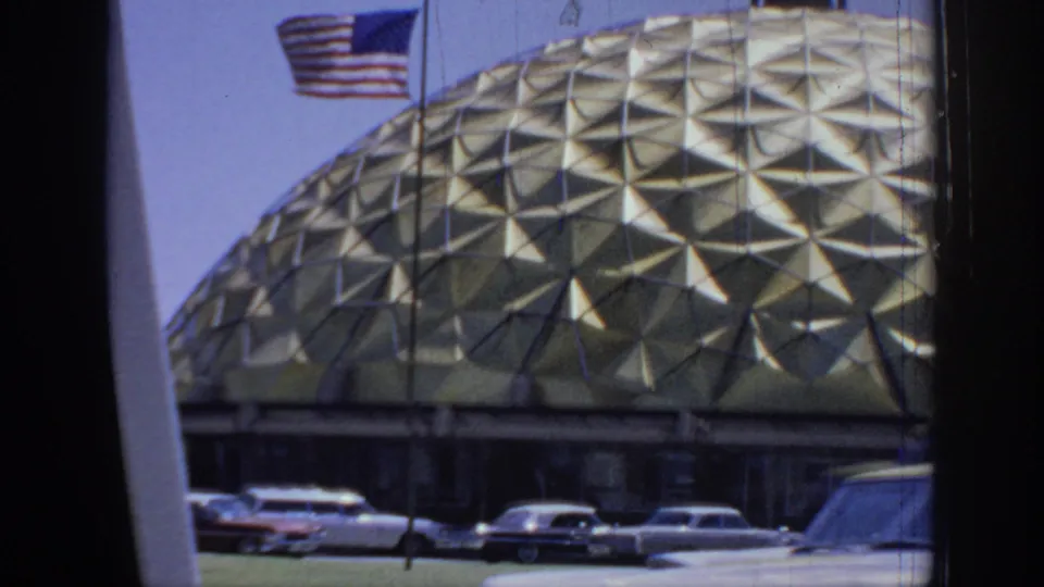1967 Oklahoma home-movie frame showing a gold triangular-pattern dome, American flag, and classic cars viewed from a vehicle.