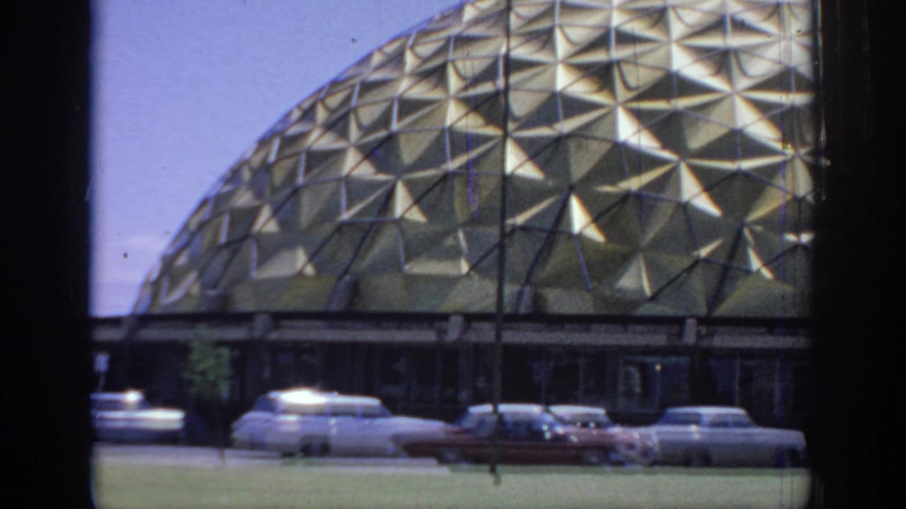Gold dome roof seen through a vehicle window with several classic cars parked below.