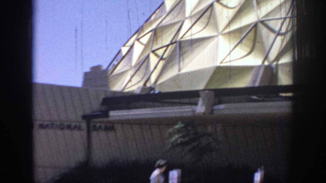 A moving 8mm view shows the dome structure over a bank wall, with partial signage, landscaping, and a woman near the lower edge.