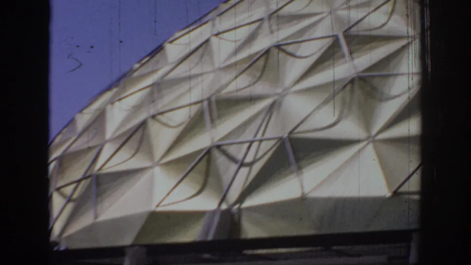 Close 8mm view of the Oklahoma dome's cream triangular panel grid, with dark frame edge and blue sky visible.