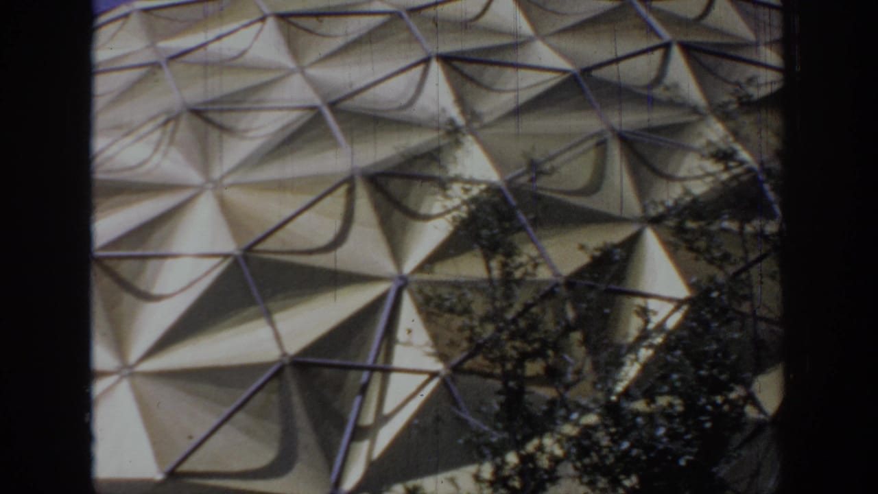 1967 Oklahoma 8mm frame showing a triangular-paneled dome exterior partly obscured by dark tree trunks and branches.