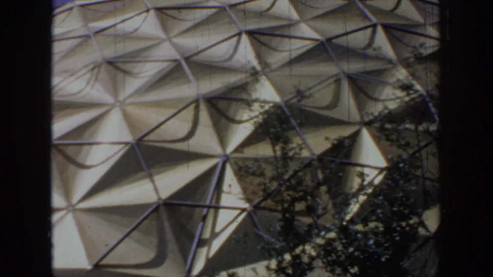 1967 Oklahoma 8mm frame showing a triangular-paneled dome exterior partly obscured by dark tree trunks and branches.