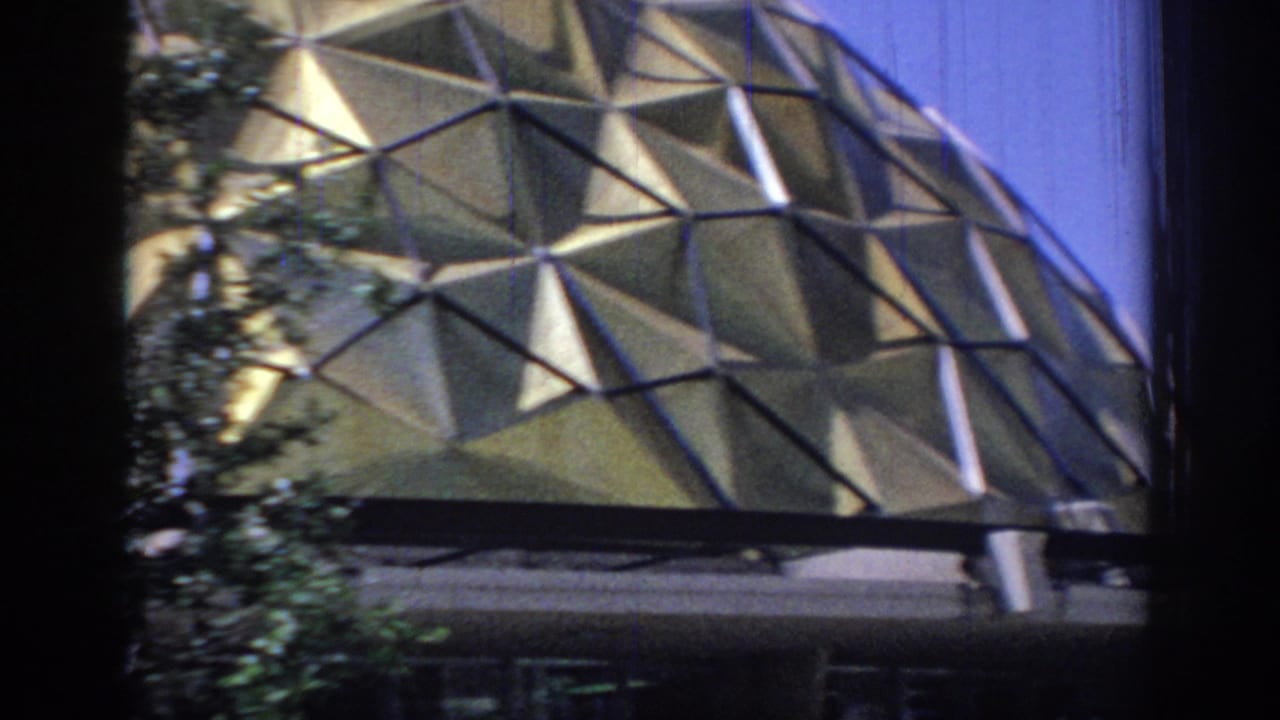 Handheld 8mm view of the lower dome panels descending toward an entrance canopy and shadowed doorway area.