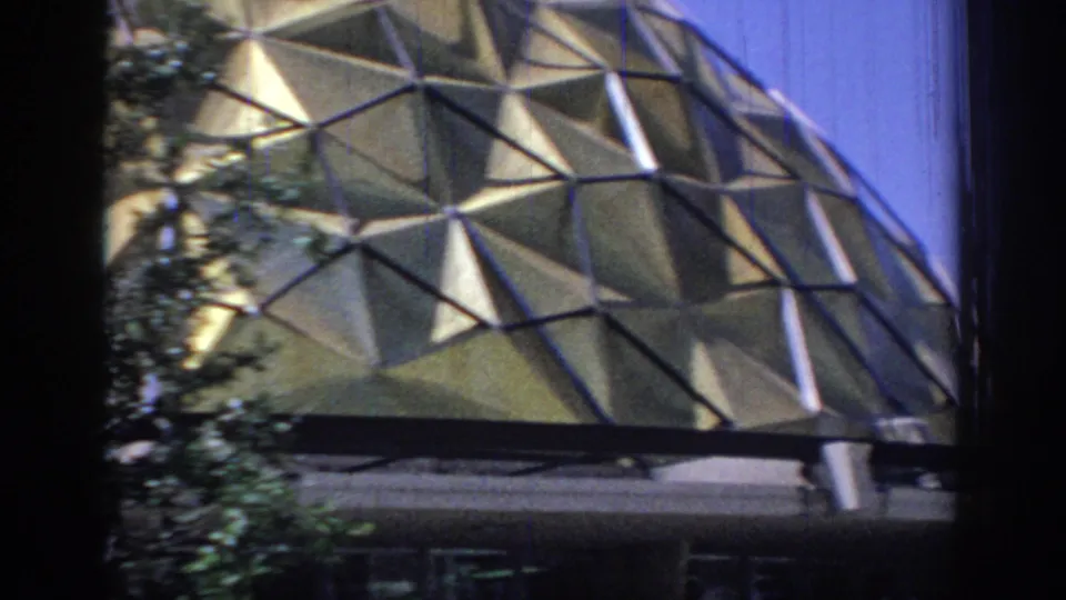 Handheld 8mm view of the lower dome panels descending toward an entrance canopy and shadowed doorway area.
