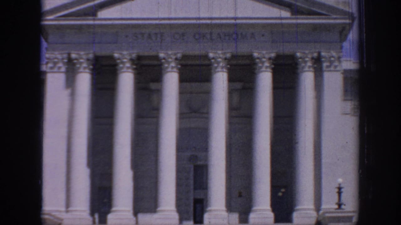 1967 8mm view of the Oklahoma State Capitol facade, showing white columns, pediment, and the engraved state name above the entrance.