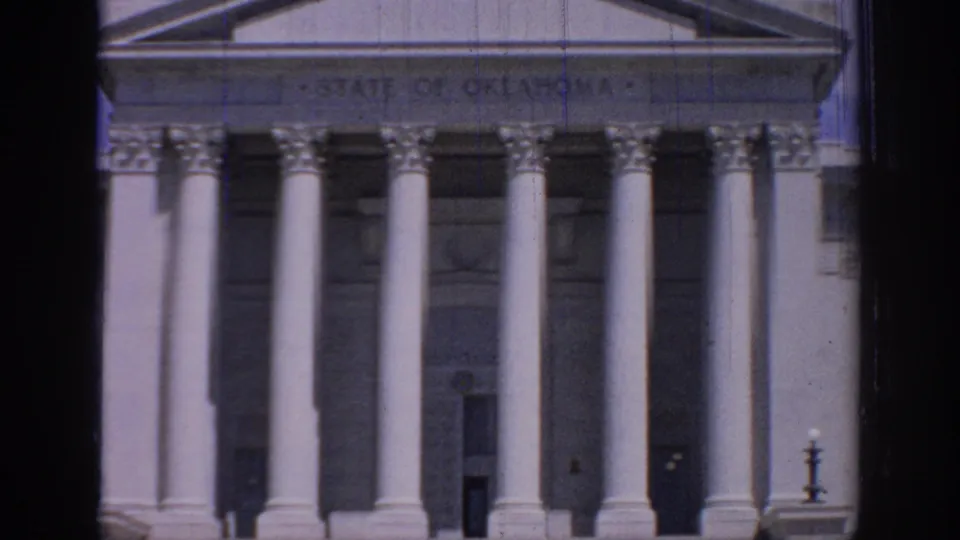 1967 8mm view of the Oklahoma State Capitol facade, showing white columns, pediment, and the engraved state name above the entrance.