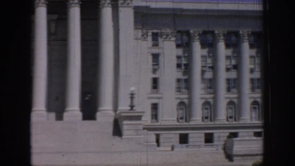 Faded 8mm view of the Oklahoma State Capitol exterior, with columns, a lamp post, stone base, and adjoining rows of windows.
