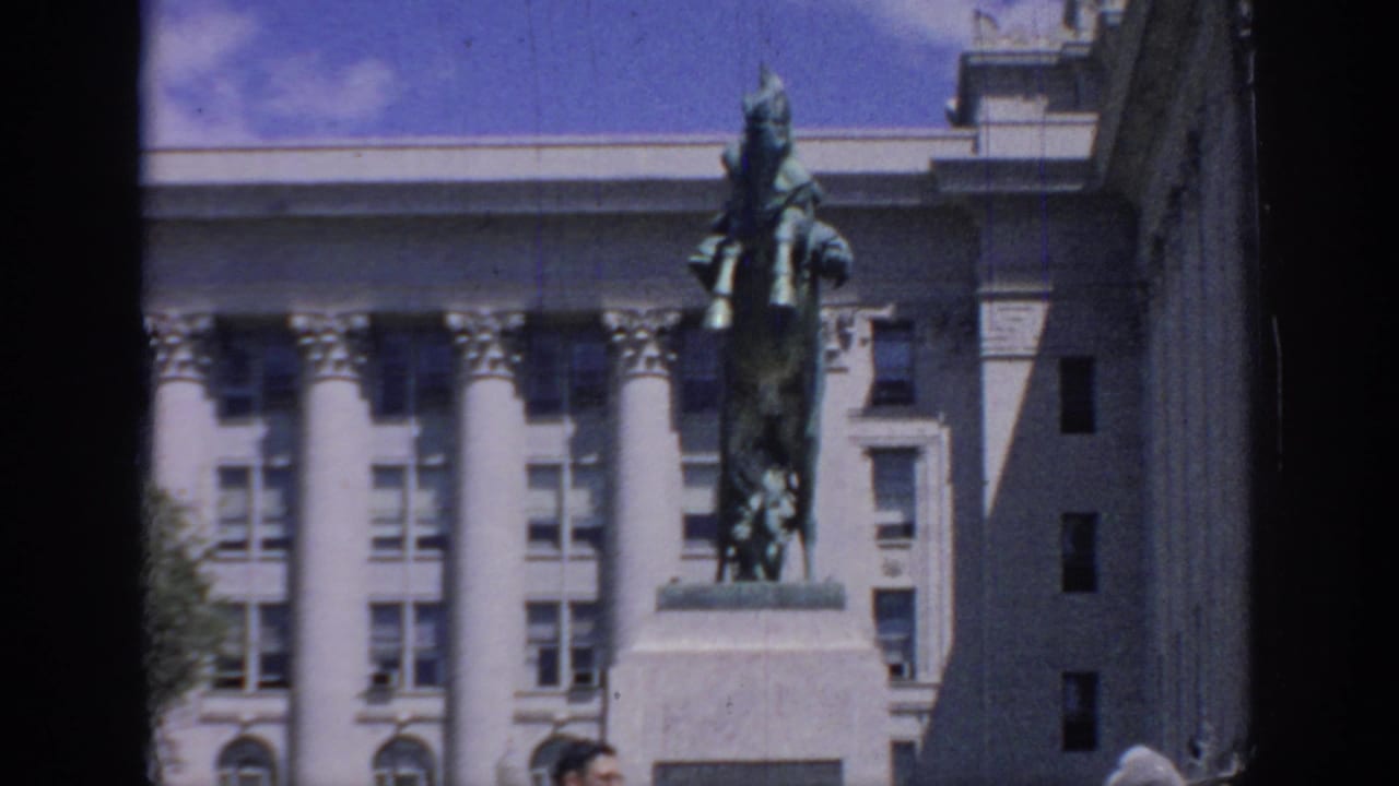 The statue and pedestal stand in bright daylight before a grand columned facade in this 1967 Oklahoma home-movie view.