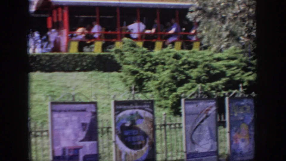 1967 Oklahoma frame with visitors in an elevated amusement ride above a row of colorful painted banners and greenery.