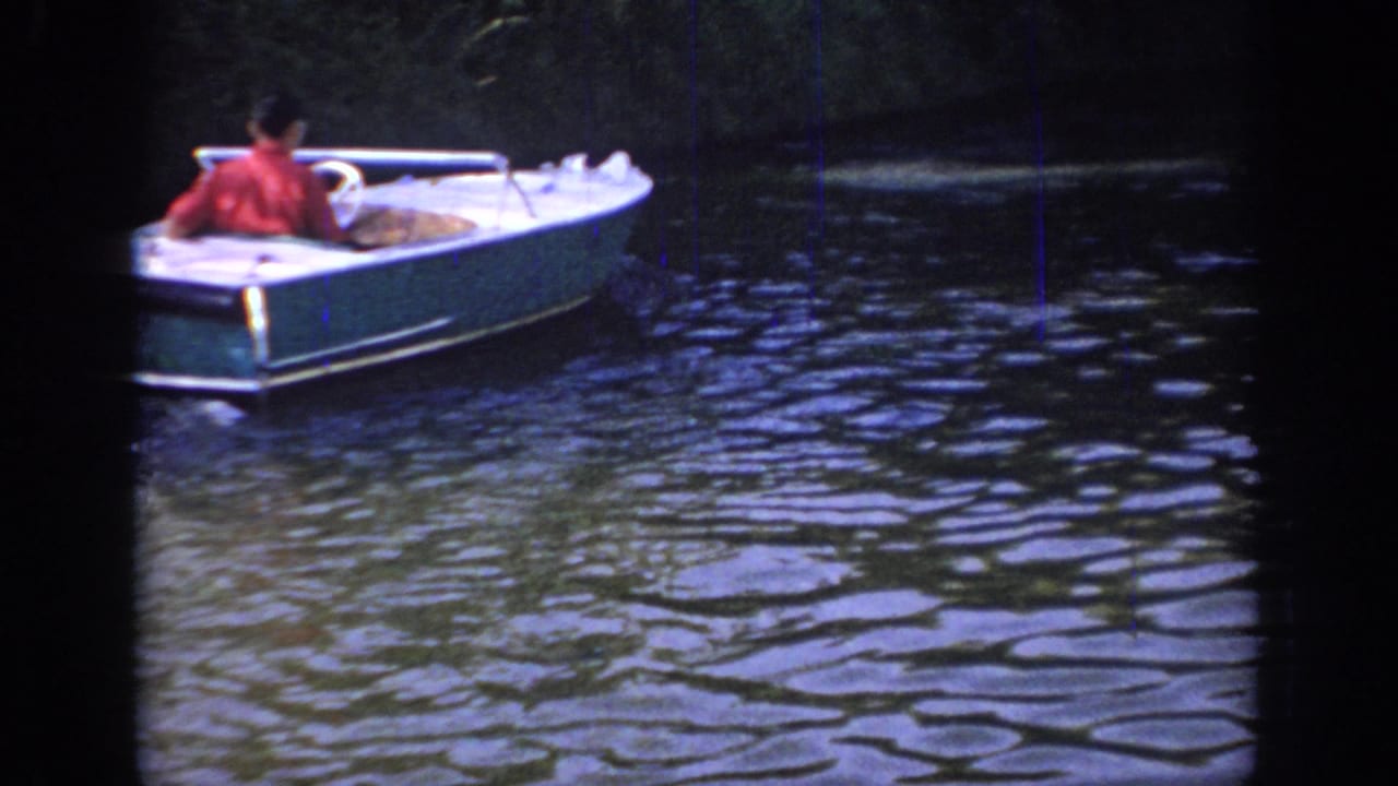 Small white motorboat with a man aboard moving across rippling water.