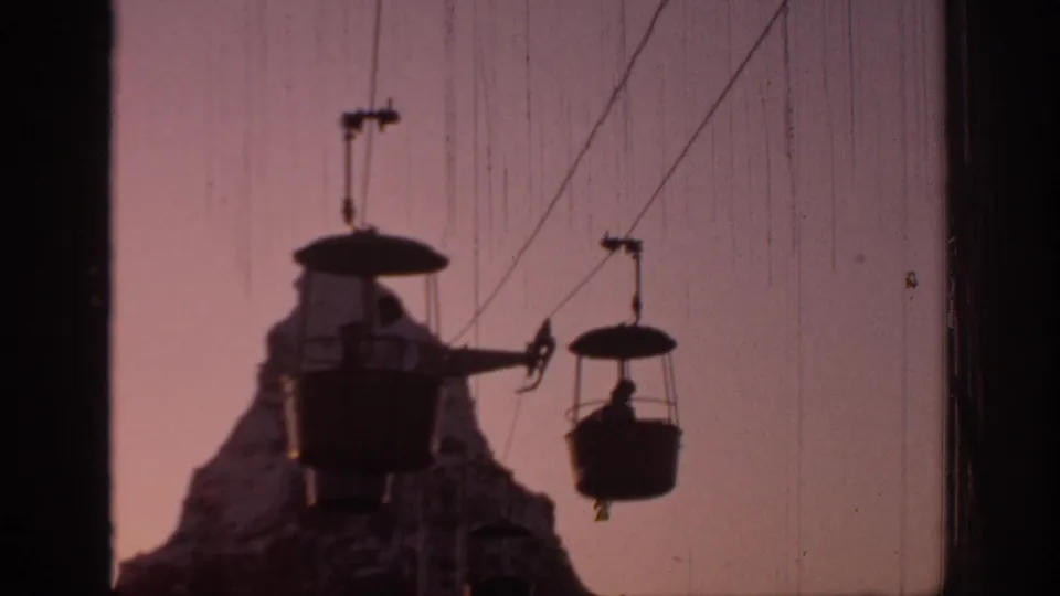 1967 Oklahoma home-movie frame showing silhouetted cable cars and riders against a pink-orange sunset sky.