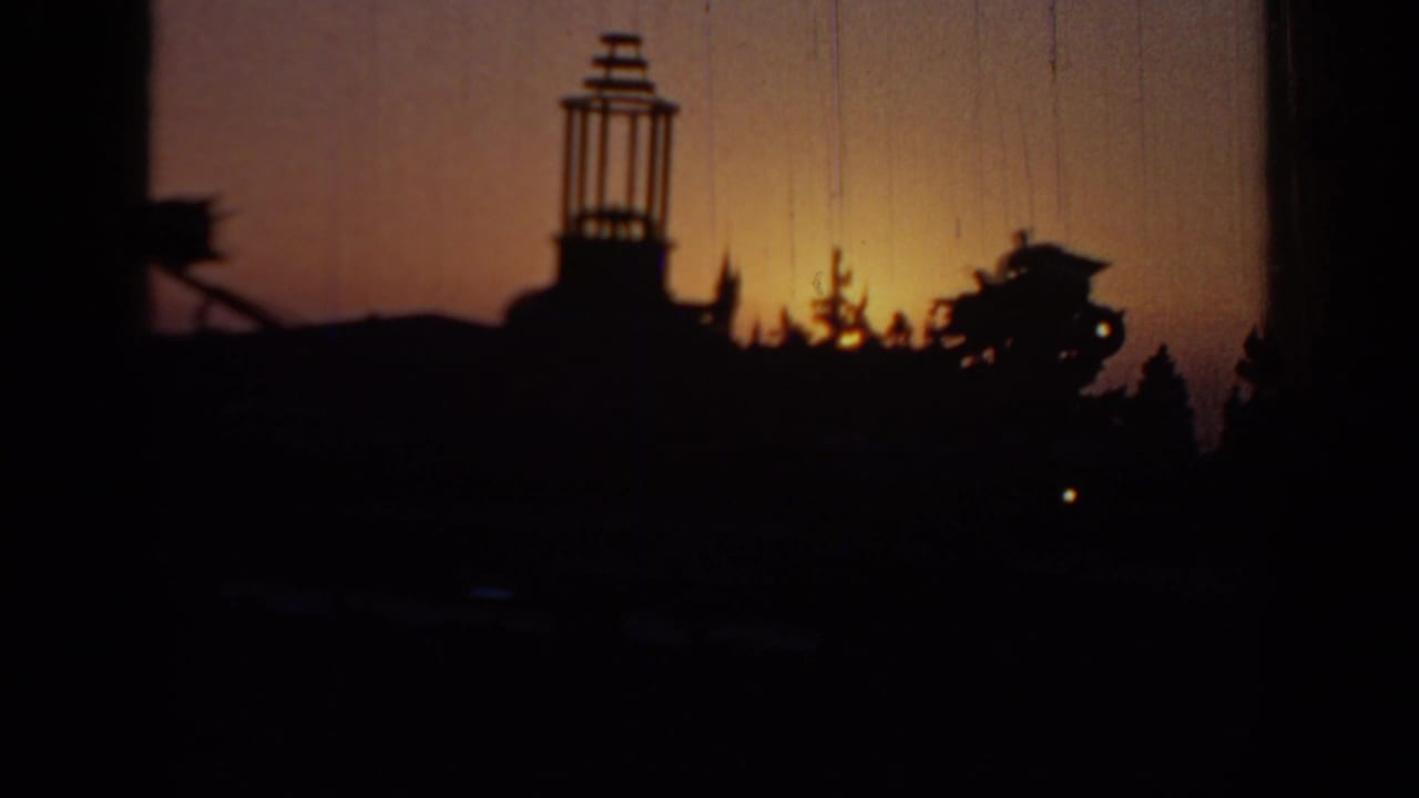 Dark amusement-park skyline with a tower-like structure silhouetted against sunset.