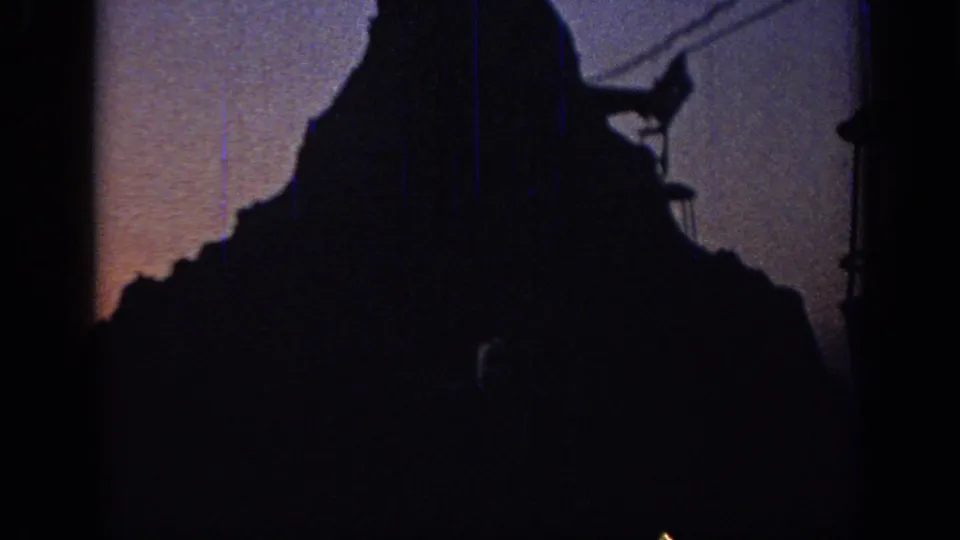 1967 Oklahoma home-movie frame with cable equipment and a large silhouetted peak shape in low light.
