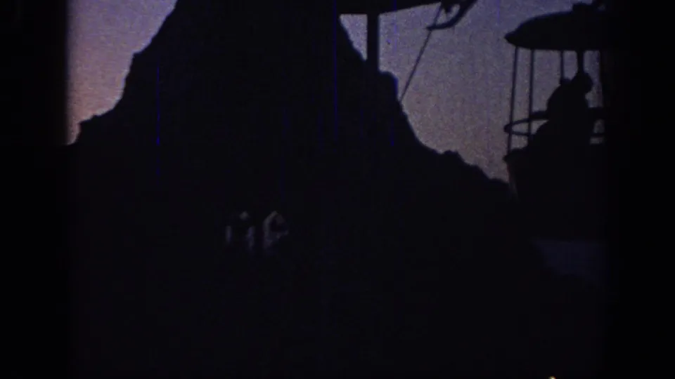 Oklahoma 1967 8mm frame with a silhouetted cable car near a dark peak, partially obscured by exposure and grain.