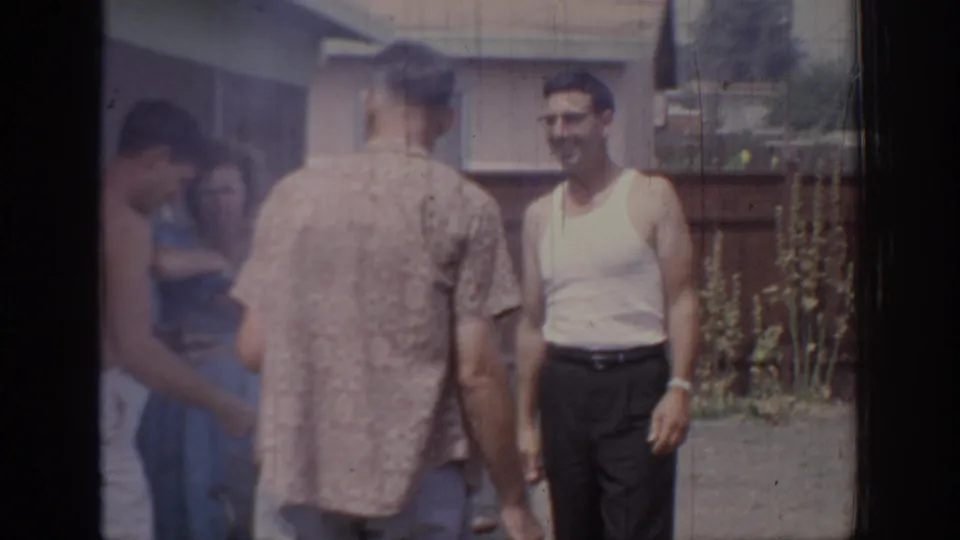 1967 Oklahoma 8mm frame showing adults in casual mid-century clothing talking outside near a house and wooden fence.