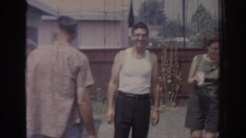 1967 Oklahoma home-movie frame with a man in a sleeveless shirt and a woman holding a drink at an outdoor gathering.