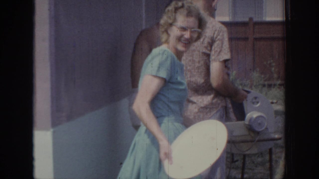 In 1967 Oklahoma home-movie footage, a woman in a light blue dress smiles beside adults near a backyard grill area.