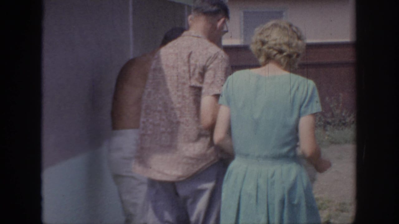 Man and woman seen from behind standing near a backyard grill and fence.