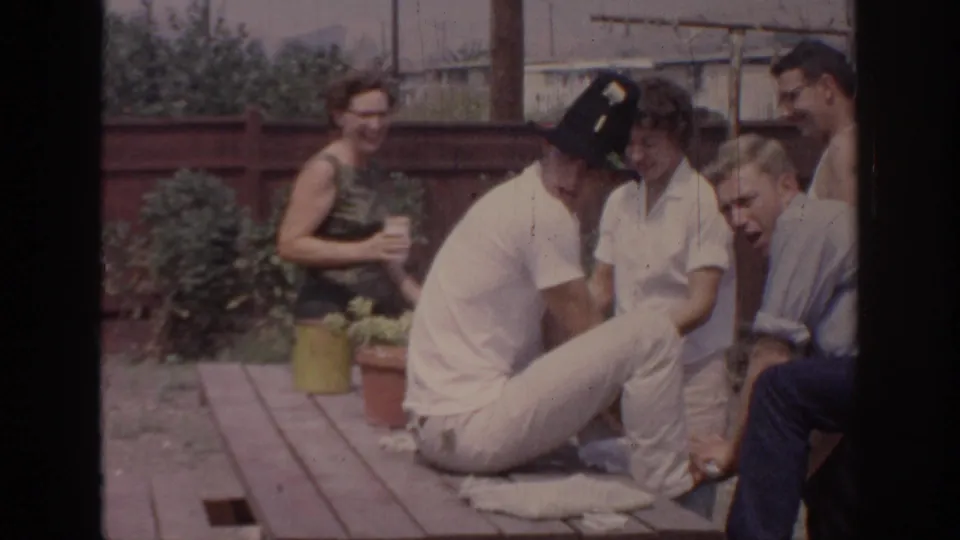 1967 Oklahoma backyard gathering with adults seated and standing around a wooden picnic table during a casual party.