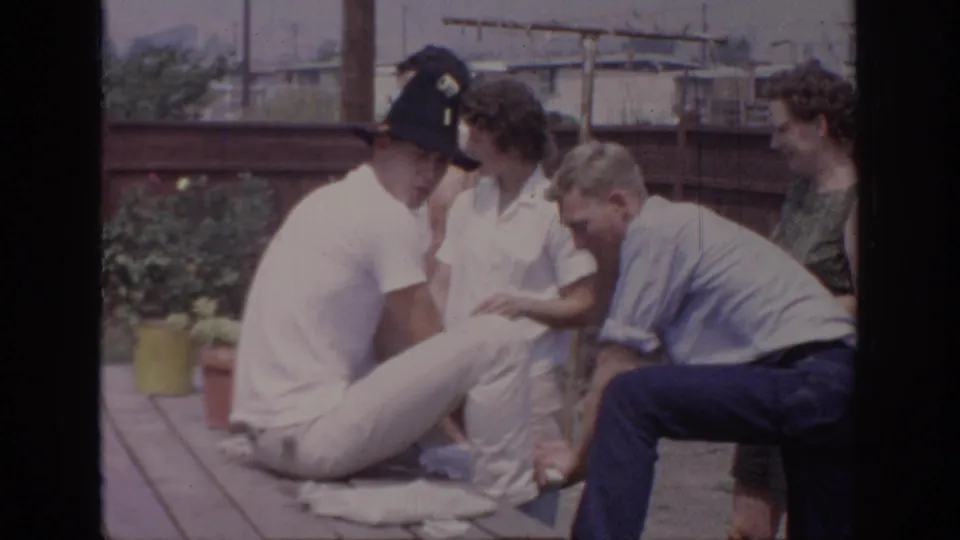 Adults in a 1967 Oklahoma backyard gather near a picnic table as a man in a black hat sits with one leg extended.