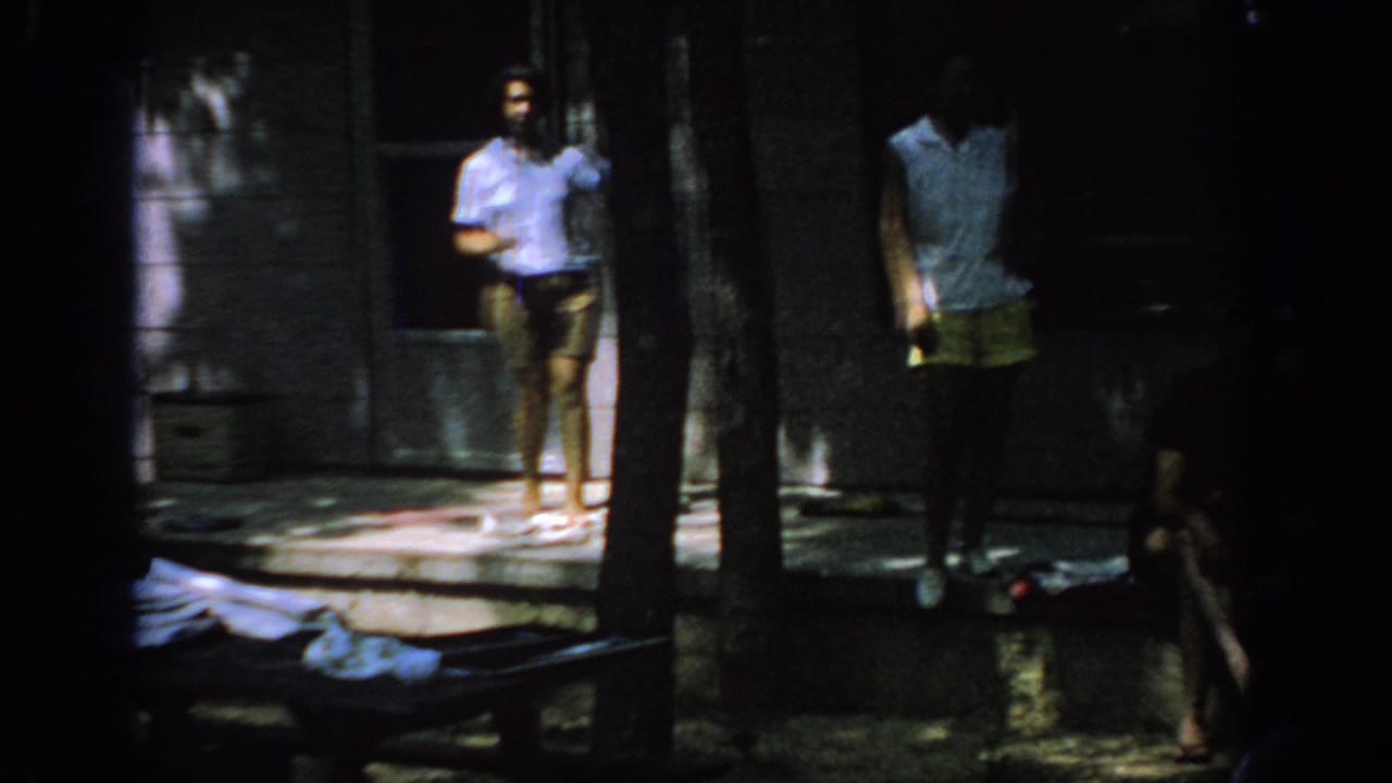 Two adults stand by a porch while another figure sits near the steps.