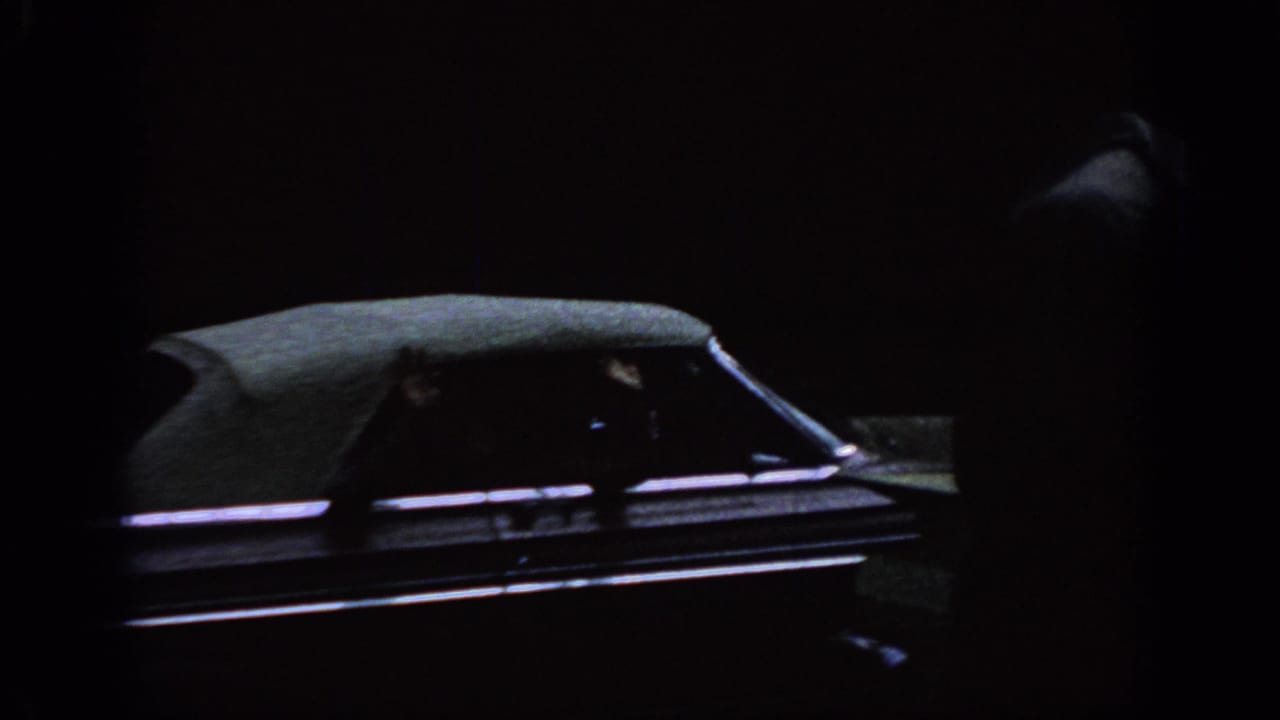 Shadowed 8mm frame showing part of a parked car before the backyard laundry scene begins.