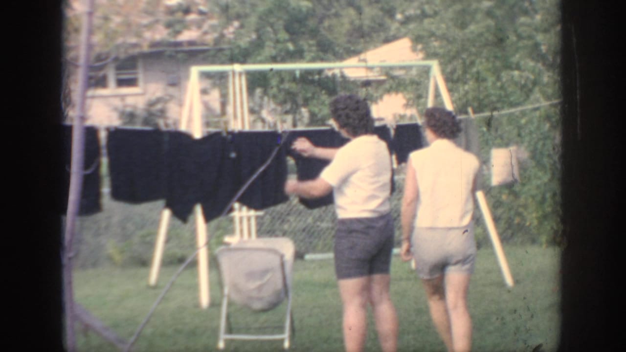 Two women stand by a backyard clothesline with dark laundry.