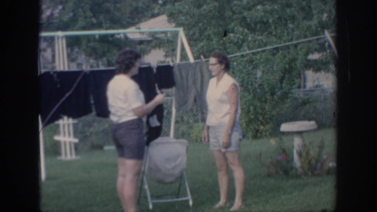 In a 1967 Oklahoma backyard, one woman handles laundry near a clothesline while another stands nearby in shorts.