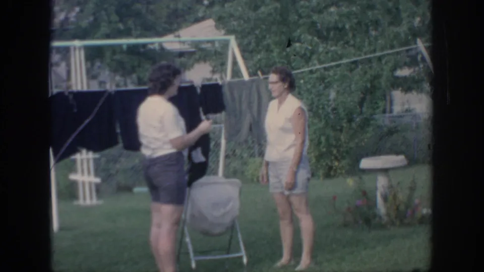 In a 1967 Oklahoma backyard, one woman handles laundry near a clothesline while another stands nearby in shorts.