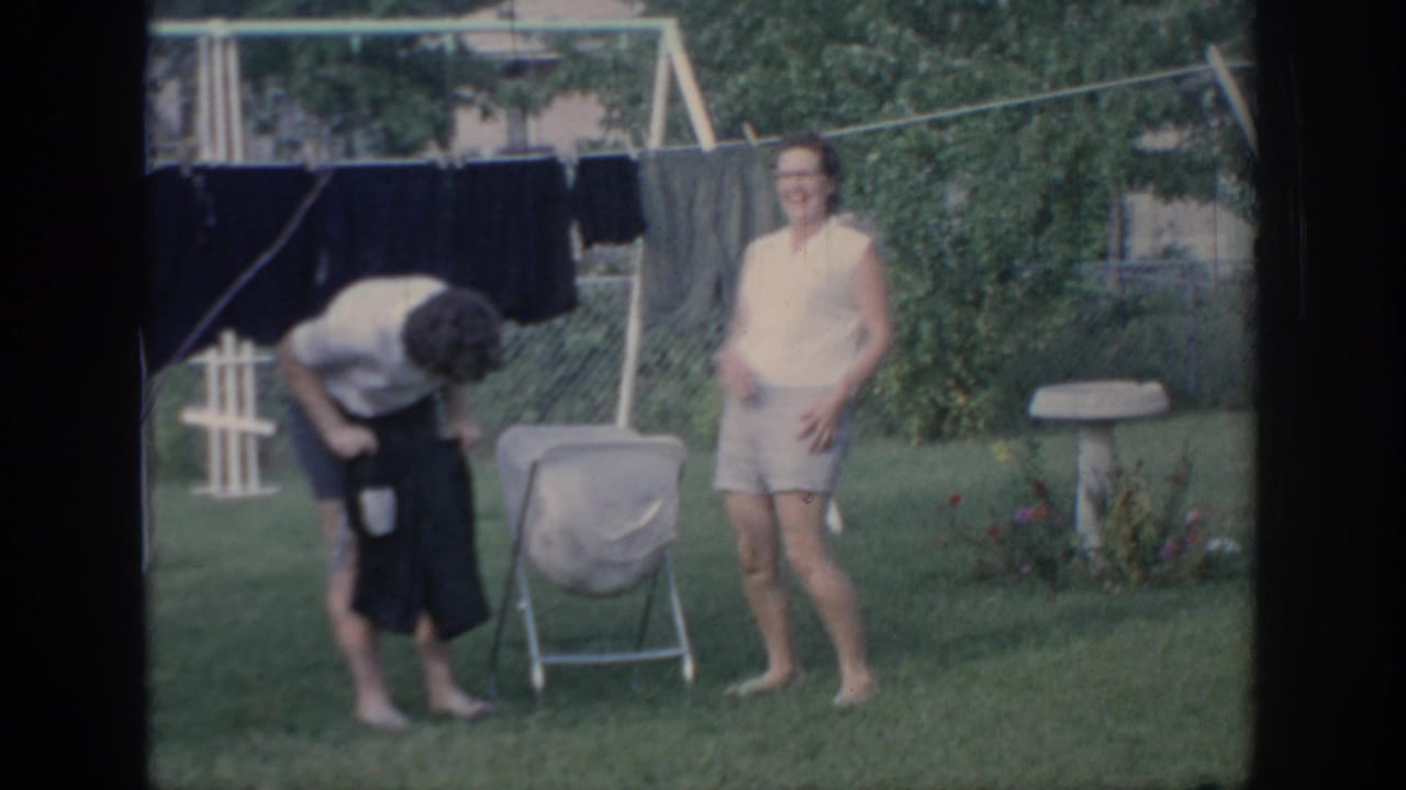 In 1967 Oklahoma home-movie footage, two women stand in a backyard as one bends near a laundry basket beside a clothesline.