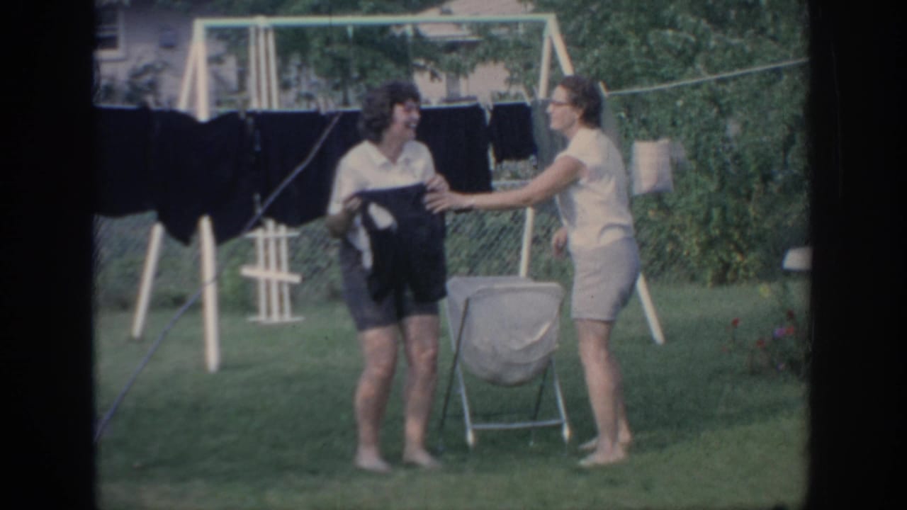 Two women laugh and interact beside a clothesline in a backyard.