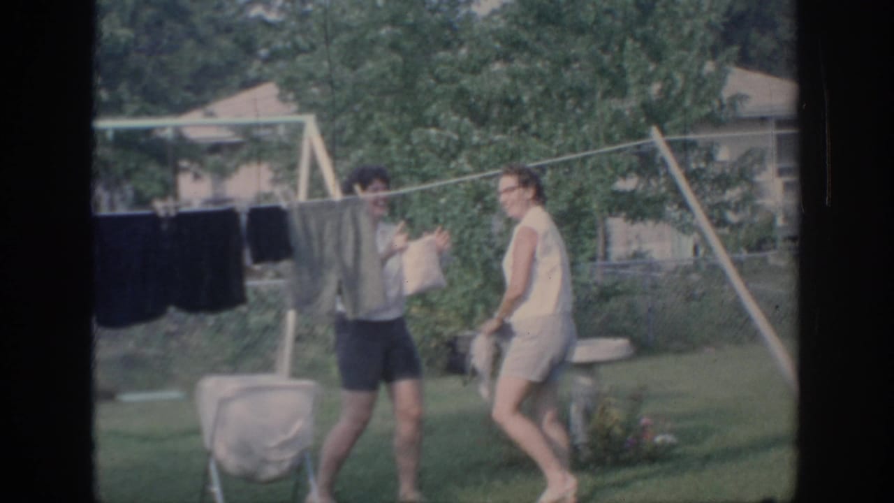 1967 Oklahoma backyard footage shows two young women interacting playfully beside a clothesline and summer lawn.