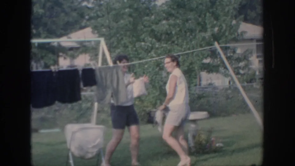 1967 Oklahoma backyard footage shows two young women interacting playfully beside a clothesline and summer lawn.