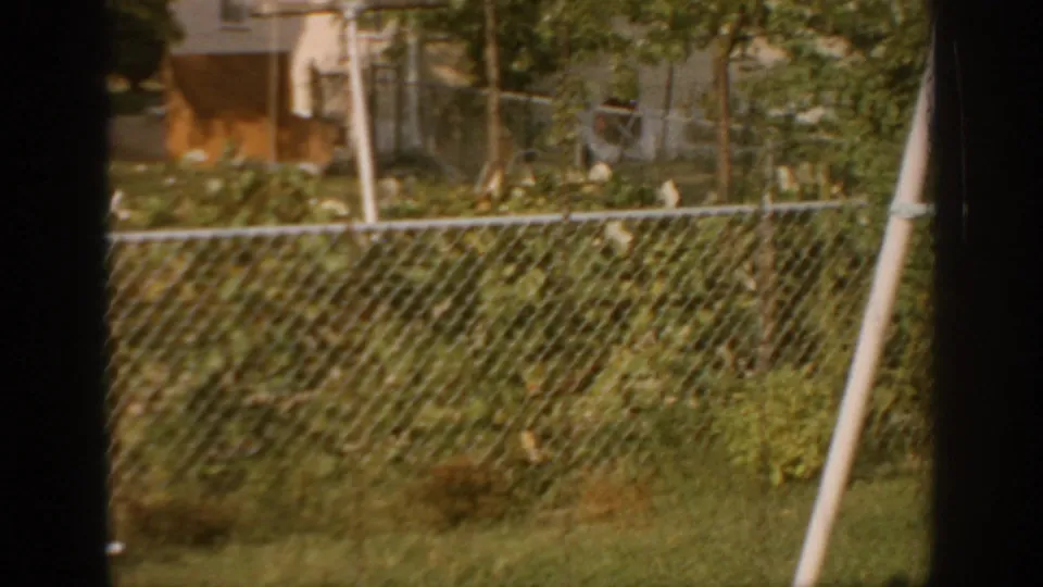 1967 Oklahoma 8mm frame looking across a backyard fence, with partial laundry, garden plants, house edges, and dark window borders.
