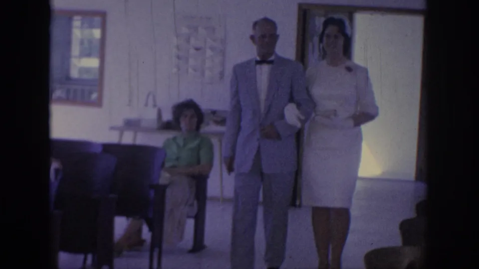 1967 Oklahoma frame of the couple walking toward the camera, with chairs, a seated observer, and a window visible in the ceremony room.