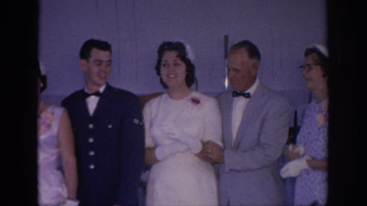 1967 Oklahoma wedding party stands indoors as the bride links arms with guests beside a groom in a dark formal uniform-style jacket.