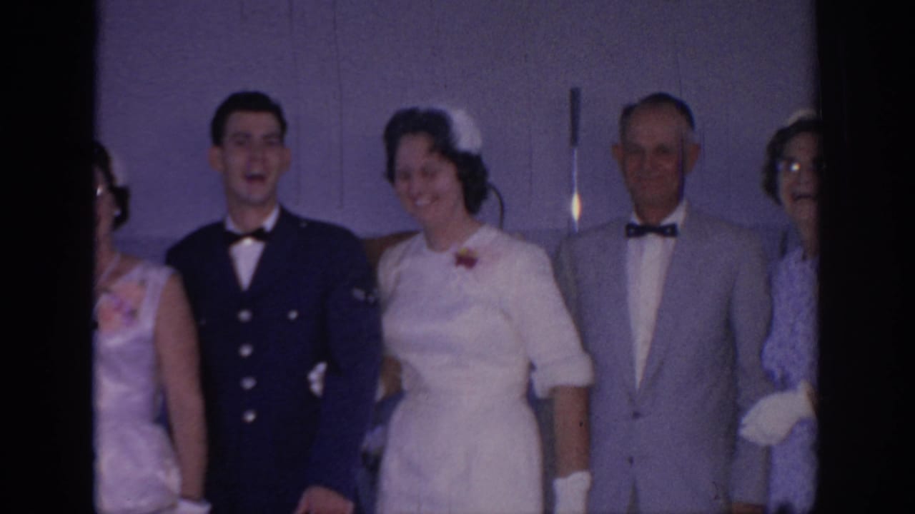 Bride and groom stand with older guests, smiling toward the camera.