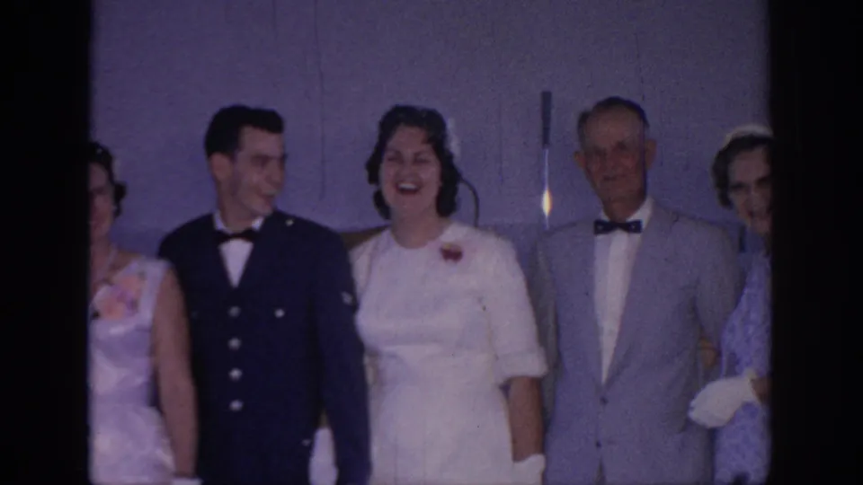 At the Oklahoma wedding, the bride laughs openly while the groom looks toward her and an older man in a gray suit faces forward.